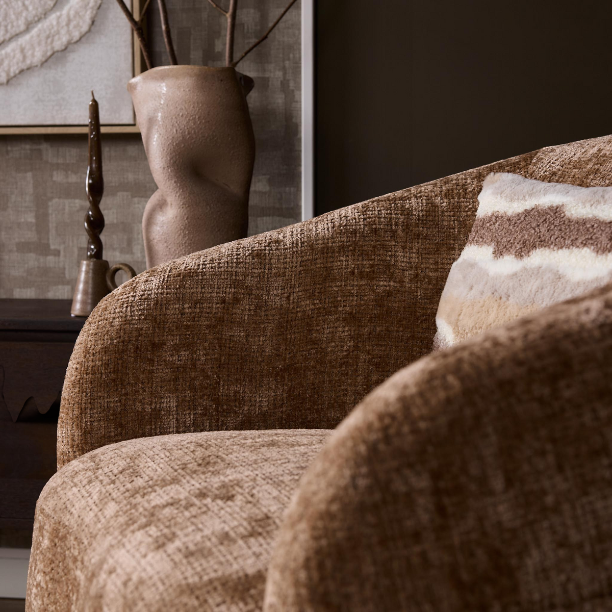 Aika draaibare fauteuil Kaze in bruine textuurstof met een gestreept sierkussen in een sfeervol interieur
